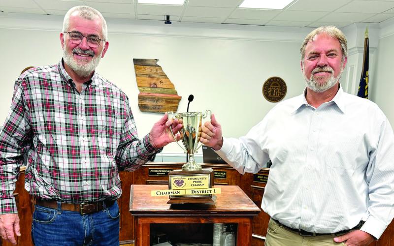 Board of Commissioners Chairman Chris Weidner (left) and Commissioner Sam Kitchens share the March 28 Clean Up trophy at the conclusion of last week’s county commission meeting. DEBBIE LURIE-SMITH/Staff