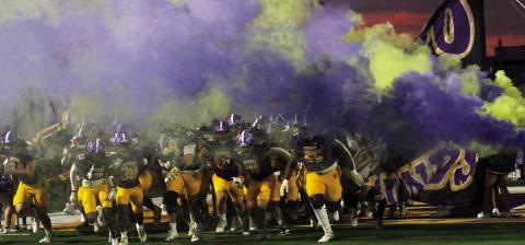 The Greyhounds rush through the run-through sign and the smoke to take the field against Stockbridge. BRAD HARRISON/Staff