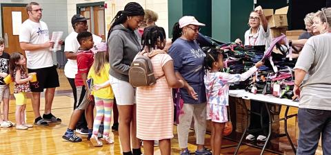 Families line up with students to receive a book bag and school supplies from volunteers with the Pilot Club of Jones County. CONTRIBUTED