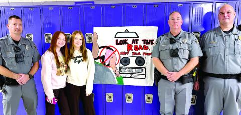 Gray Police Officers Michael Holloway (l-r), Henry Thayer and Capt. Jacob Hunnicutt with JCHS students Ella Carr and Jamie Cocking surrounding the driver safety posters displayed in the halls of Jones County High School. DEBBIE LURIE-SMITH/Staff