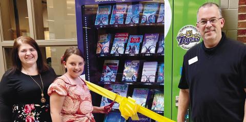Laura Dixon, media specialist, and Jeffrey Tharpe, principal, have a fifth-grade student, Ava Rogers, cut the ribbon for the book vending machine. ALAINA CLARKE/Staff