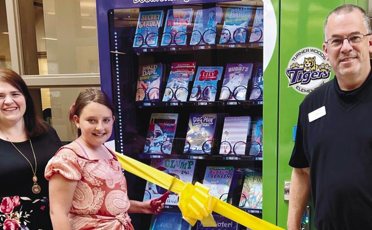 Laura Dixon, media specialist, and Jeffrey Tharpe, principal, have a fifth-grade student, Ava Rogers, cut the ribbon for the book vending machine. ALAINA CLARKE/Staff